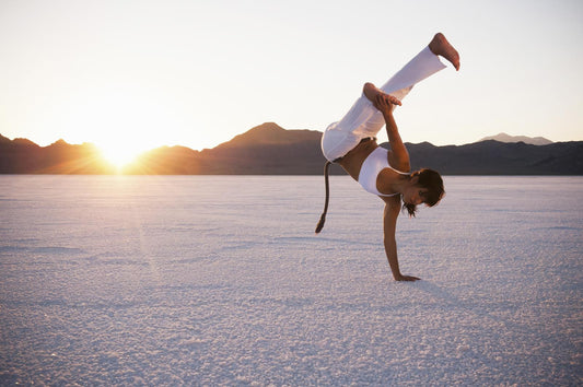 Woman performing an acrobatic one-arm handstand on a salt flat